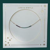 Necklace on a card with 'June & Simple' branding against a dark green background