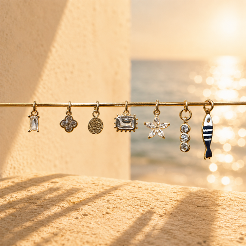 Seven gold-filled charm options for a build-your-own necklace, shown on a bar by the sea