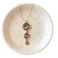 A gold-filled chain drop necklace with a crushed natural abalone shell pendant, displayed on a ceramic plate with a white and gold color scheme.