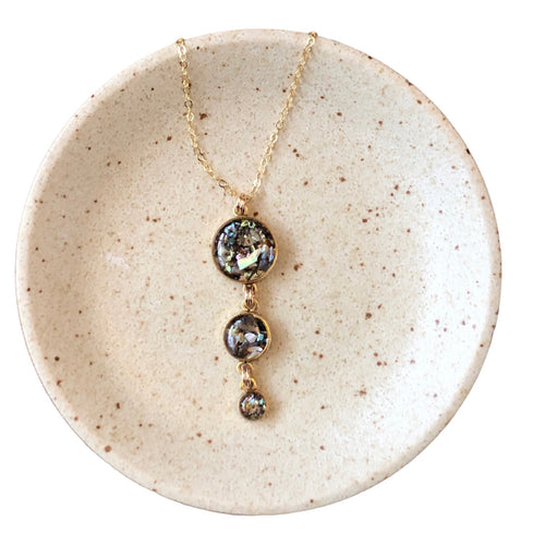 A gold-filled chain drop necklace with a crushed natural abalone shell pendant, displayed on a ceramic plate with a white and gold color scheme.